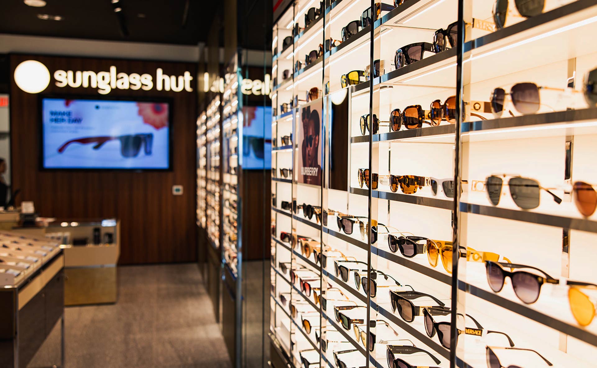 Sunglass Hut store interior with a backlit wall of sunglasses