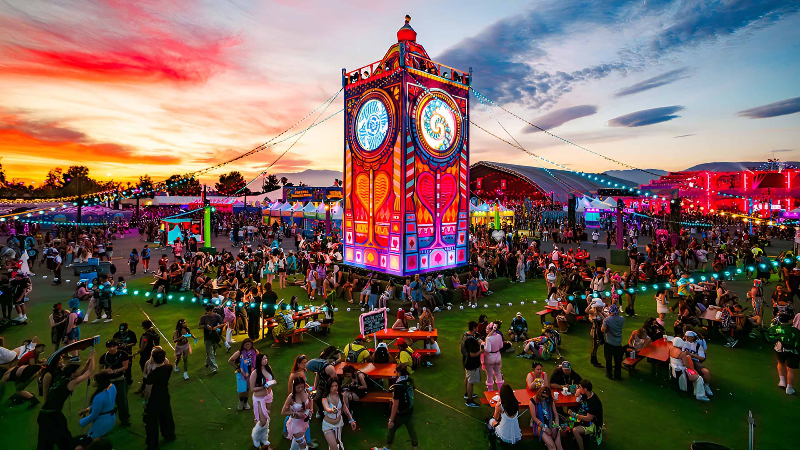 Illuminated clock-tower centrepiece over the festival grounds at sunset